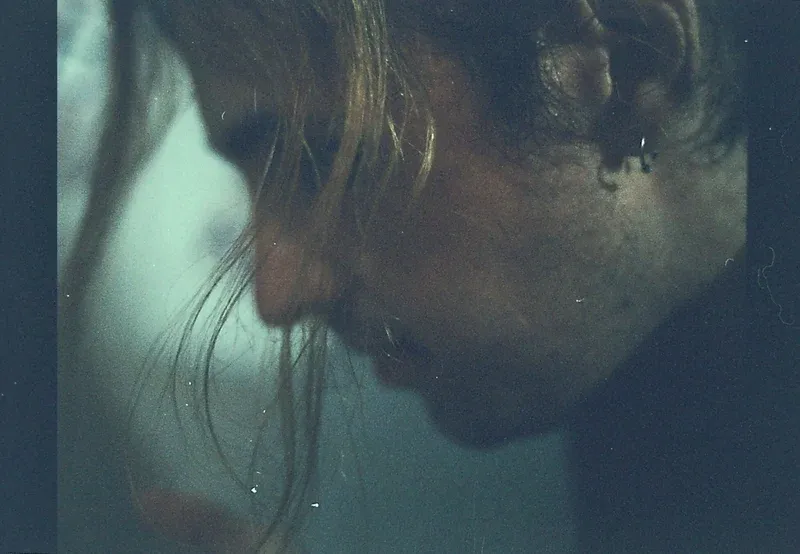 Close-up portrait in muted blue-green light, with visible film grain
